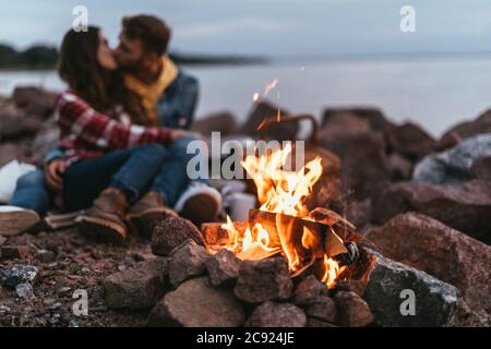 Selektiver Fokus von brennendem Lagerfeuer in der Nähe von Paar küssen und auf Felsen sitzen Stockfoto