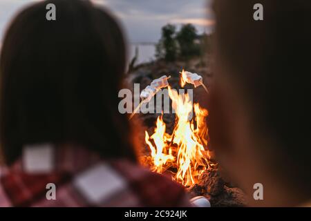 Selektiver Fokus von geschwollenen Marshmallows auf Stöcken in der Nähe von Lagerfeuer und Paar Stockfoto