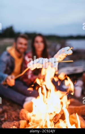 Selektive Konzentration von geschwollenen Marshmallows auf Stöcke in der Nähe brennender Lagerfeuer und Paar Stockfoto