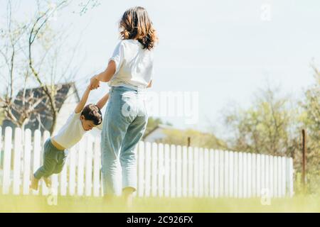 Rückansicht der Mutter, die Hände mit dem Sohn hält und Zeit draußen verbringt Stockfoto