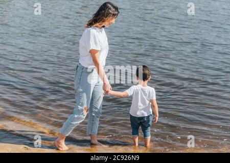 Glückliche Mutter hält Hände mit niedlichen Sohn und steht im See Stockfoto