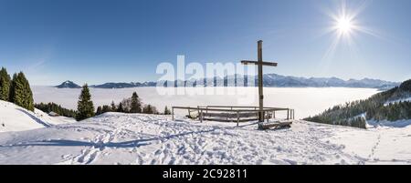 Gipfelkreuz auf Schneeberg mit blauem Himmel und Sonne. Toller Blick auf die Bergkette über der Nebelschicht des Inversionstales. Ofterschwanger Horn, Alpen, Allgau Stockfoto