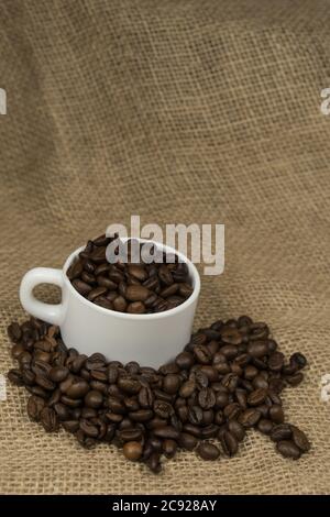 Frisch zubereiteter Kaffee in einer weißen Tasse, umgeben von Kaffeebohnen auf einem Holztisch. Frischer Kaffee. Stockfoto