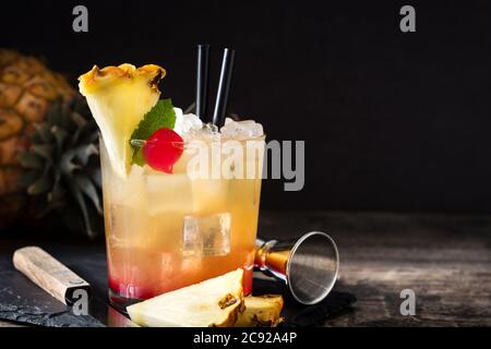 Kalter Mai Tai Cocktail mit Ananas und Kirsche im Glas auf schwarzem Hintergrund Stockfoto