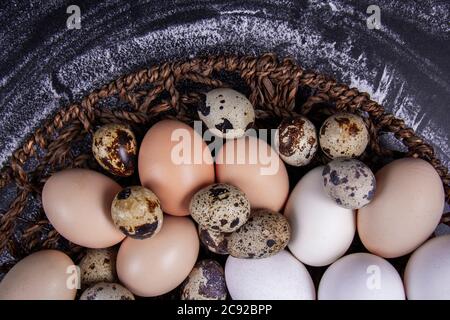 Einige gesunde einheimische Eier und Wachteleier befinden sich in einem Holzkorb neben einem Holzlöffel. Stockfoto