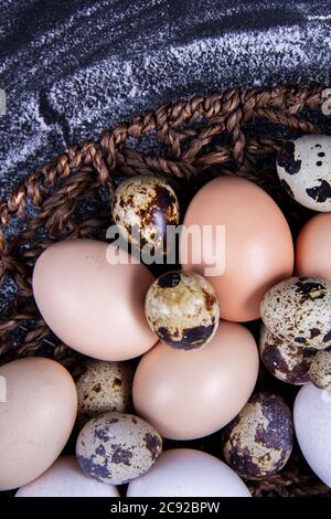 Einige gesunde einheimische Eier und Wachteleier befinden sich in einem Holzkorb neben einem Holzlöffel. Stockfoto