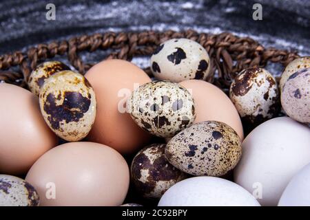 Einige gesunde einheimische Eier und Wachteleier befinden sich in einem Holzkorb neben einem Holzlöffel. Stockfoto