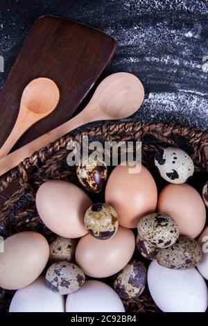Einige gesunde einheimische Eier und Wachteleier befinden sich in einem Holzkorb neben einem Holzlöffel. Stockfoto