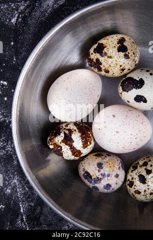 Einige gesunde einheimische Eier und Wachteleier befinden sich in einem Holzkorb neben einem Holzlöffel. Stockfoto