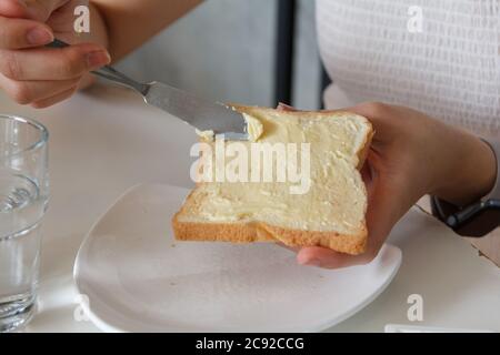 Nahaufnahme der weiblichen Hände, die Butter auf Brot verteilen Stockfoto