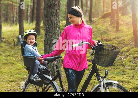 Glückliche Mutter mit Sohn in Fahrrad Kindersitz Radfahren auf Waldweg Stockfoto