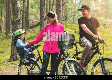 Junge glückliche Familie Radfahren im Wald mit Kind in Fahrrad Kindersitz. Aktive Sport Outdoor-Erholung Stockfoto