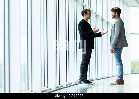 Zwei Geschäftsleute, die sich in einem Büro mit Fenstern und Blick auf die Stadt in einer Diskussion befinden Stockfoto