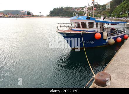 Abendlicht mit Reflexionen in ruhigem Wasser mit einem festgezurrenen blauen Fischerboot in Ribadesella Asturias Spanien Stockfoto