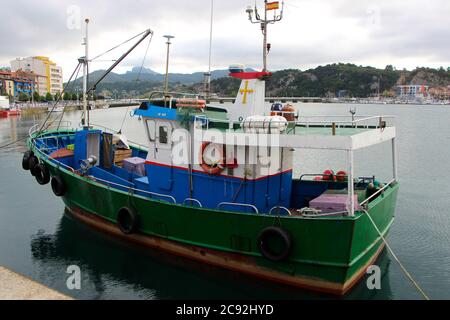 Abendlicht mit Reflexionen in ruhigem Wasser mit einem grün blau und weiß anlegeenden Fischerboot in Ribadesella Asturias Spanien Stockfoto
