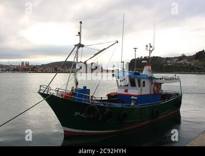 Abendlicht mit Reflexionen in ruhigem Wasser mit einem grün blau und weiß anlegeenden Fischerboot in Ribadesella Asturias Spanien Stockfoto