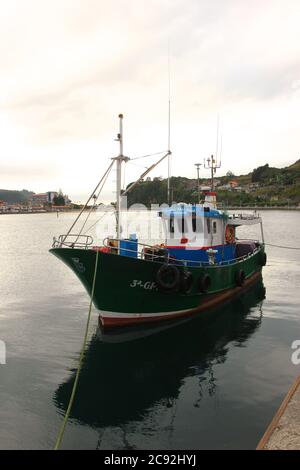 Abendlicht mit Reflexionen in ruhigem Wasser mit einem grün blau und weiß anlegeenden Fischerboot in Ribadesella Asturias Spanien Stockfoto