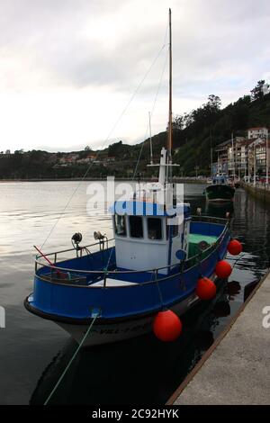Abendlicht mit Reflexionen in ruhigem Wasser mit einem festgezurrenen blauen Fischerboot in Ribadesella Asturias Spanien Stockfoto