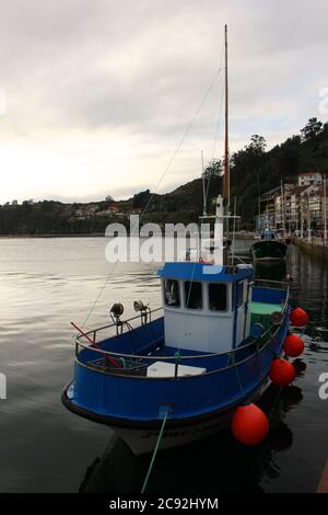 Abendlicht mit Reflexionen in ruhigem Wasser mit einem festgezurrenen blauen Fischerboot in Ribadesella Asturias Spanien Stockfoto