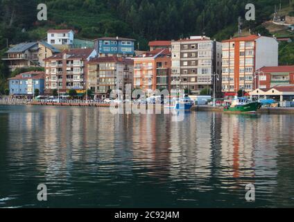 Abendlicht mit Reflexionen in ruhigem Wasser mit einem festgezurrenen blauen Fischerboot in Ribadesella Asturias Spanien Stockfoto