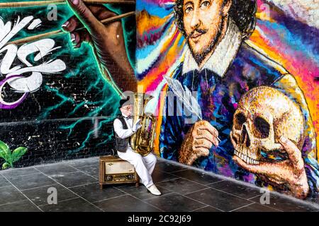 Ein Street Entertainer spielt Musik vor EINEM riesigen Wandbild von William Shakespeare, Clink Street, London, Großbritannien Stockfoto