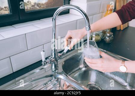Frau, die das Glas mit Wasser aus dem Stahlhahn füllte In der Küche Stockfoto