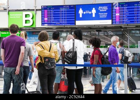 Dortmund, 28. Juli 2020: Passagiere am Flughafen Dortmund tragen vor der Sicherheitskontrolle Mund- und Nasenschutz im Abflugterminal. Die Anzeigetafel zeigt den Sicherheitsabstand an --- Dortmund, 28.07.2020: Dortmund Airport, Passagiere tragen Mund-Nasenschutz im Terminal Abflug vor dem Security Check. Die Anzeigetafel weißt auf Sicherheitsabstand hin. Stockfoto