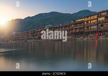 Traditionelle alte Holzstelzenhäuser am Ufer des Flusses Tuo, die an einem ruhigen, ruhigen Morgen im Sommer durch das Zentrum der Feng huang Altstadt fließen, Stockfoto