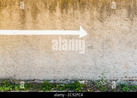 Pfeil mit einer weißen Linie auf einer Steinwand mit negativem Raum und Kopierraum gemalt, um die Richtung anzuzeigen. Stockfoto