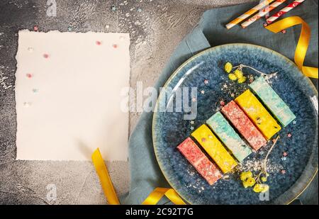 Bunte Marshmallows auf einem blauen Teller mit Bändern, Blumen und weißem Laken Stockfoto