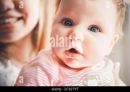 Nahaufnahme eines Neugeborenen, das in den Händen der Mutter auf die Kamera schaut. Familie zu Hause. Kleine Tochter und Mutter. Glückliche liebevolle fröhliche Familie. Stockfoto