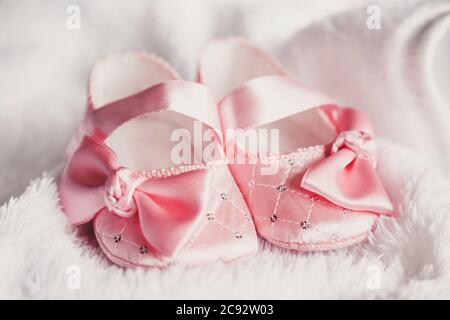 Kleidung für Neugeborene. Ein Paar niedliche babyrosa Schuhe mit Schleife für Mädchen auf einem weißen Bett. Stockfoto