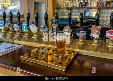 Ein Pint Bitter auf einer Kneipentheke mit einer großen Auswahl an Pumpengriffen dahinter. Stockfoto