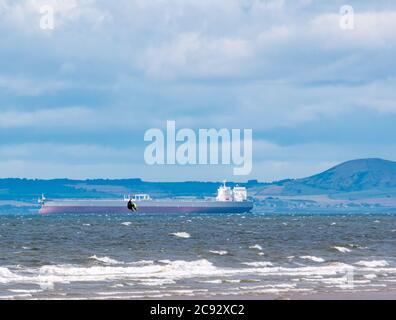 Firth of Forth, Schottland, Großbritannien, 28th. Juli 2020. Wetter in Großbritannien: Ein sehr windiger Tag bietet ideale Bedingungen für einen Kite-Surfer, der mit dem in der Ferne verankerten Tanker Aphrodite aus dem Wasser springt Stockfoto