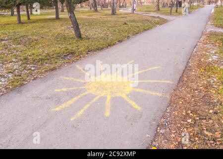 Sonne mit Strahlen gezeichnet von gelber Kreide auf Asphalt in einem städtischen Herbstpark Stockfoto