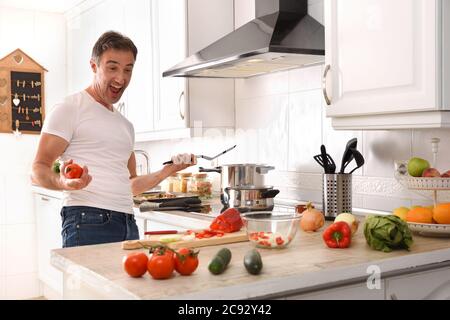 Glücklicher und ausdrucksstarker Mann, der gerne Gemüse zu Hause in einer Wohnküche kocht Stockfoto