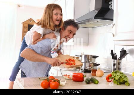 Lustige Szene von Mann Kochen und Tochter auf dem Rücken in der Küche zu Hause Stockfoto