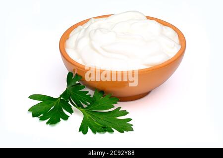 Saure Sahne, Joghurt oder weicher Quark in einer Keramikschale und Petersilienblatt isoliert auf weißem Hintergrund. Natürliche Milchprodukte. Volle Schärfentiefe. Stockfoto