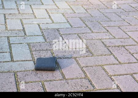 Die verlorene schwarze Brieftasche liegt auf einer leichten Pflasterplatte. Stockfoto