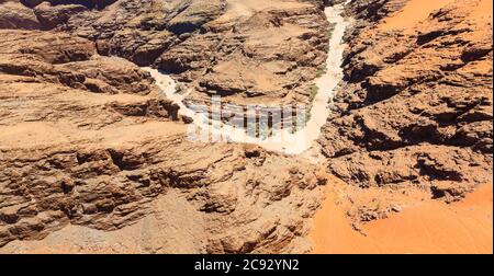 Typischer ausgetrockneter Flussbett-Wasserlauf in trockenem, trockenem Bergland der Namib-Wüste mit ockerfarbenem Sand auf geschichteten Felsen an der Skeleton Coast, Namibia, Südwestafrika Stockfoto