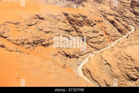 Typischer ausgetrockneter Flussbett-Wasserlauf in trockenem, trockenem Bergland der Namib-Wüste mit ockerfarbenem Sand auf geschichteten Felsen an der Skeleton Coast, Namibia, Südwestafrika Stockfoto