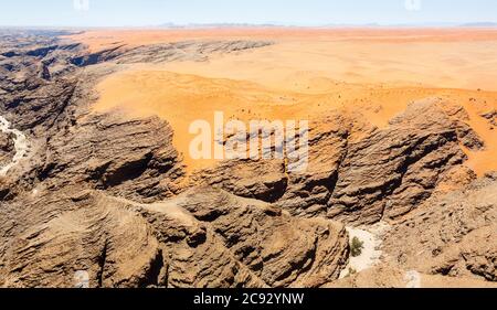 Typischer ausgetrockneter Flussbett-Wasserlauf in trockenem, trockenem Bergland der Namib-Wüste mit ockerfarbenem Sand auf geschichteten Felsen an der Skeleton Coast, Namibia, Südwestafrika Stockfoto