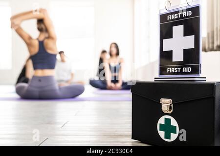 Erste-Hilfe-Box mit seiner Beschilderung für die Sicherheit im Fitness-Studio mit Hintergrund der Yoga-Klasse Studenten und Trainer. Gesunder Lebensstil und Sicherheit erster Sport Stockfoto