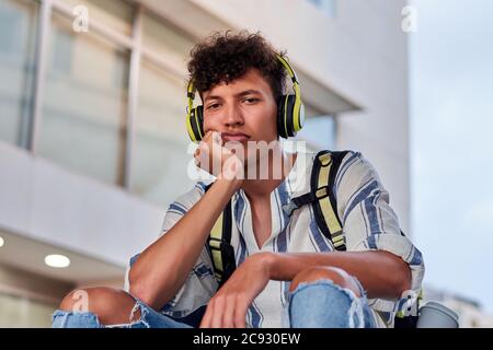 Langweiliger junger Afro mit Kopfhörern auf der Straße sitzend Stockfoto