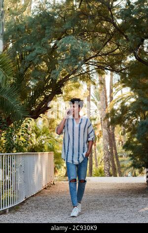 Der junge afrohaarige Mann geht und telefoniert In einem Park Stockfoto