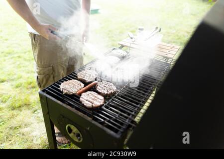 Mann steht umkippen Burger und Hotdogs auf rauchigen Hinterhof Grill Stockfoto