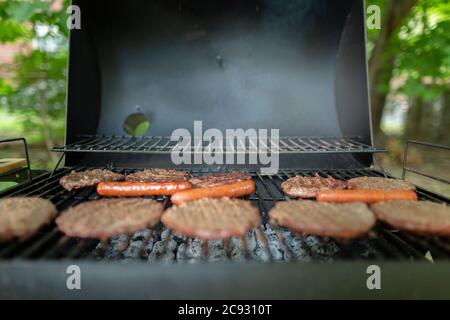 Nahaufnahme von Burgern und Hotdogs beim Kochen auf dem Holzkohlegrill im Hinterhof Stockfoto