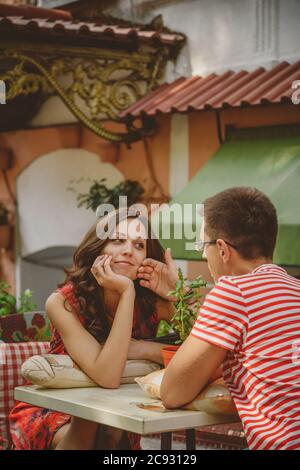 Junge schöne glücklich liebende Paar sitzt auf der Straße Open-Air-Café Blick auf einander. Beginn der Liebesgeschichte. Beziehung Liebe, Lebensstil Stockfoto