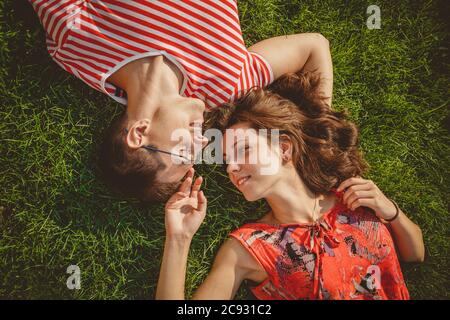 Junge liebevolle Paar zusammen liegend Kopf an Kopf auf einem Gras im Sommer. Familienpicknick. Sowohl in roter Kleidung als auch in Händen. Draufsicht Stockfoto