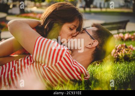 Schönes Paar liegt auf grünem Gras im Park, küssen und verbringen Zeit zusammen Stockfoto